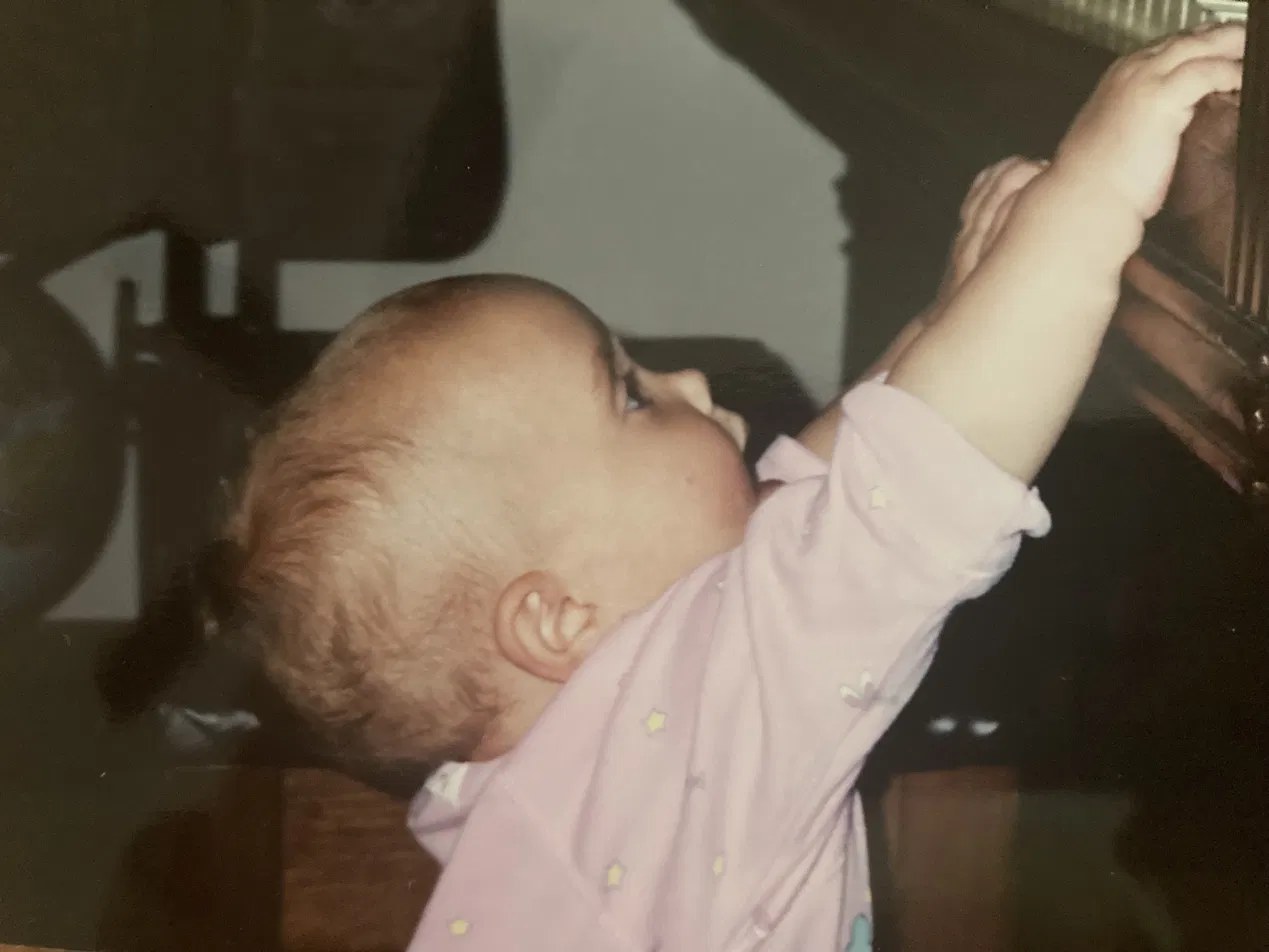 Faye as a baby reaching up to play the piano keys